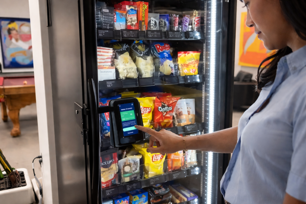 A woman is using a vending machine to buy various snacks in a public space.